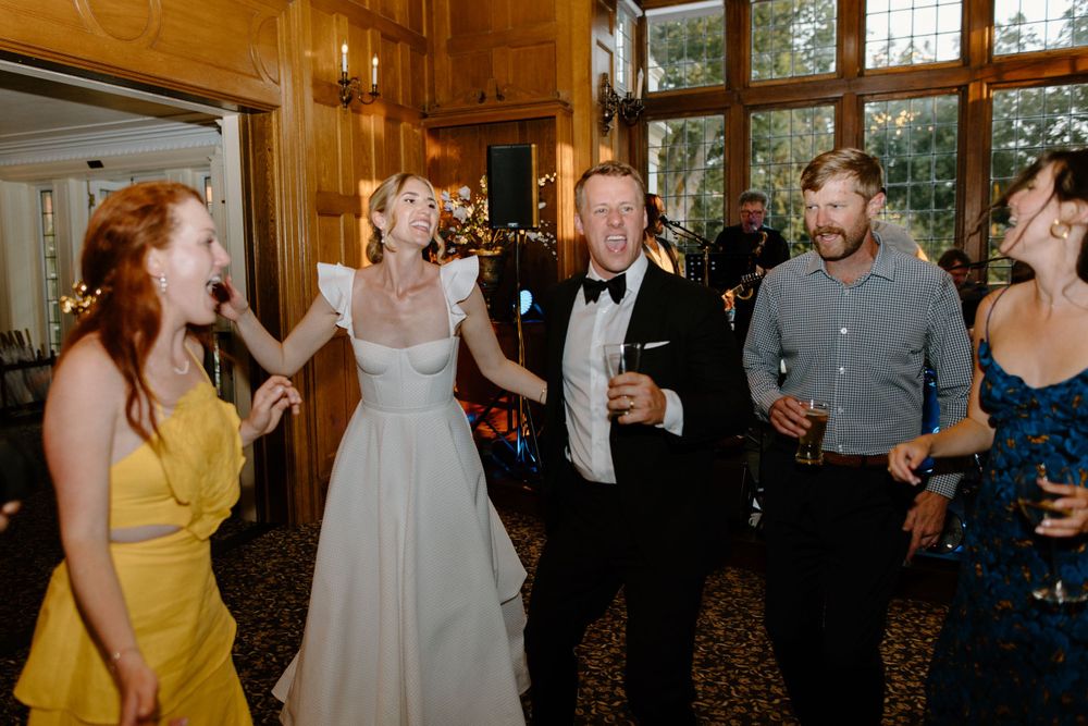Guests dancing and celebrating together at an indoor wedding reception with wood-paneled walls.