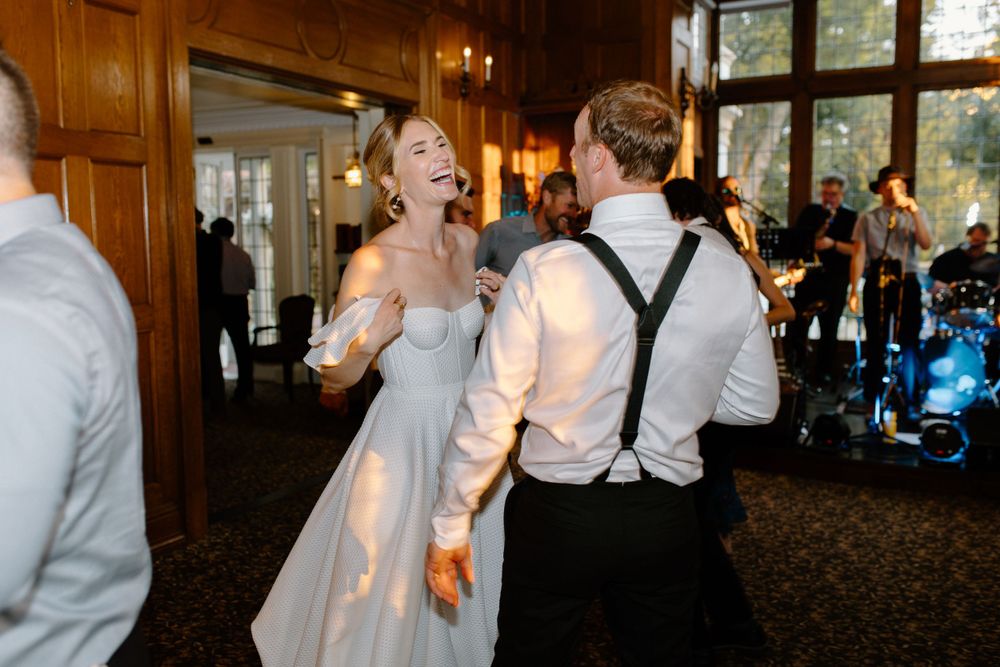A couple shares a joyful moment together on the dance floor at a wedding reception in a rustic wood-paneled venue.