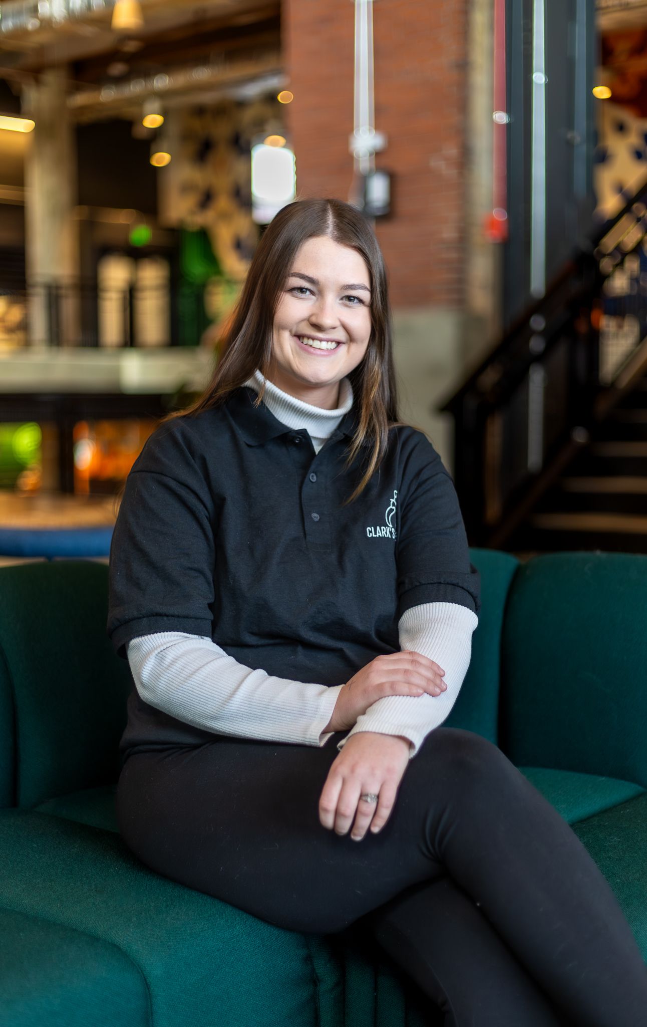 Someone wearing a black polo shirt and white undershirt sits comfortably on a green couch in a modern restaurant setting.