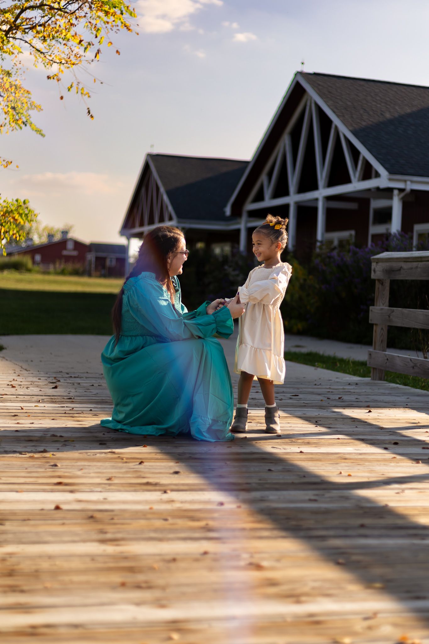 Two people share a tender moment at sunset on a wooden deck with charming lodge buildings in the background.