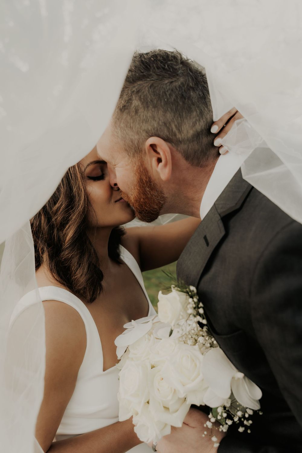 Intimate wedding portrait with white bouquet against neutral background.