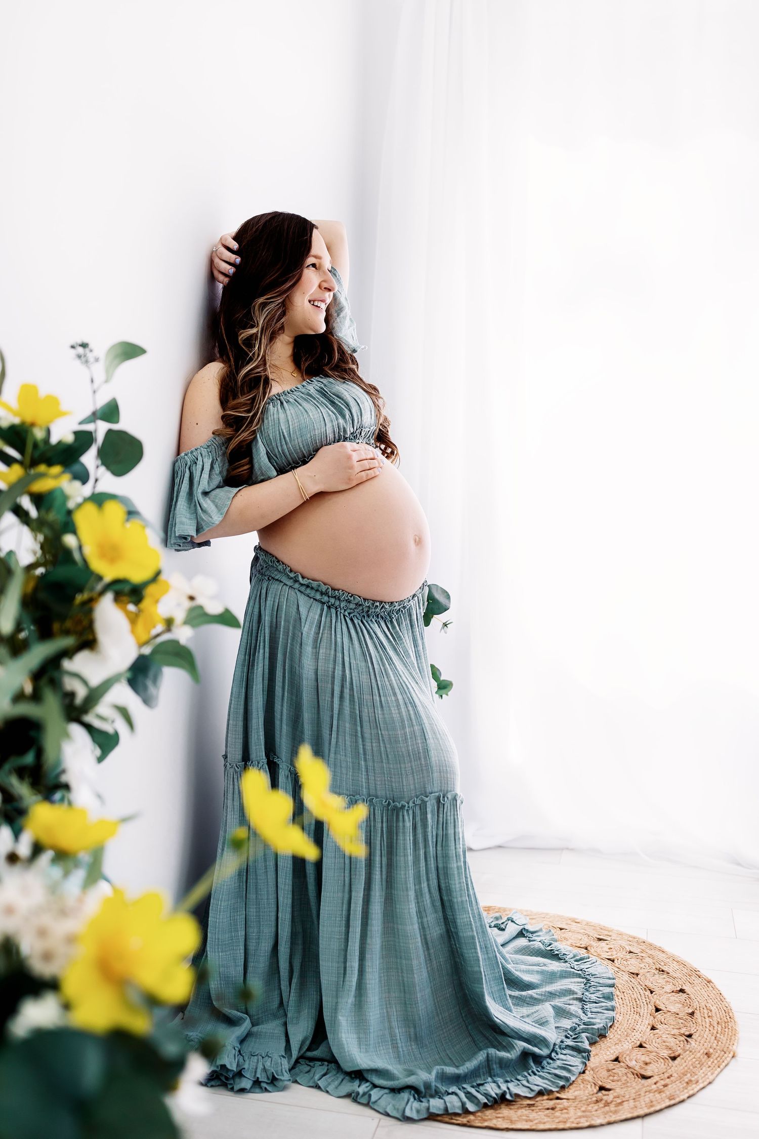 Maternity session captured by Samantha Ann Photography in a sage green dress poses in the all-white natural light studio.