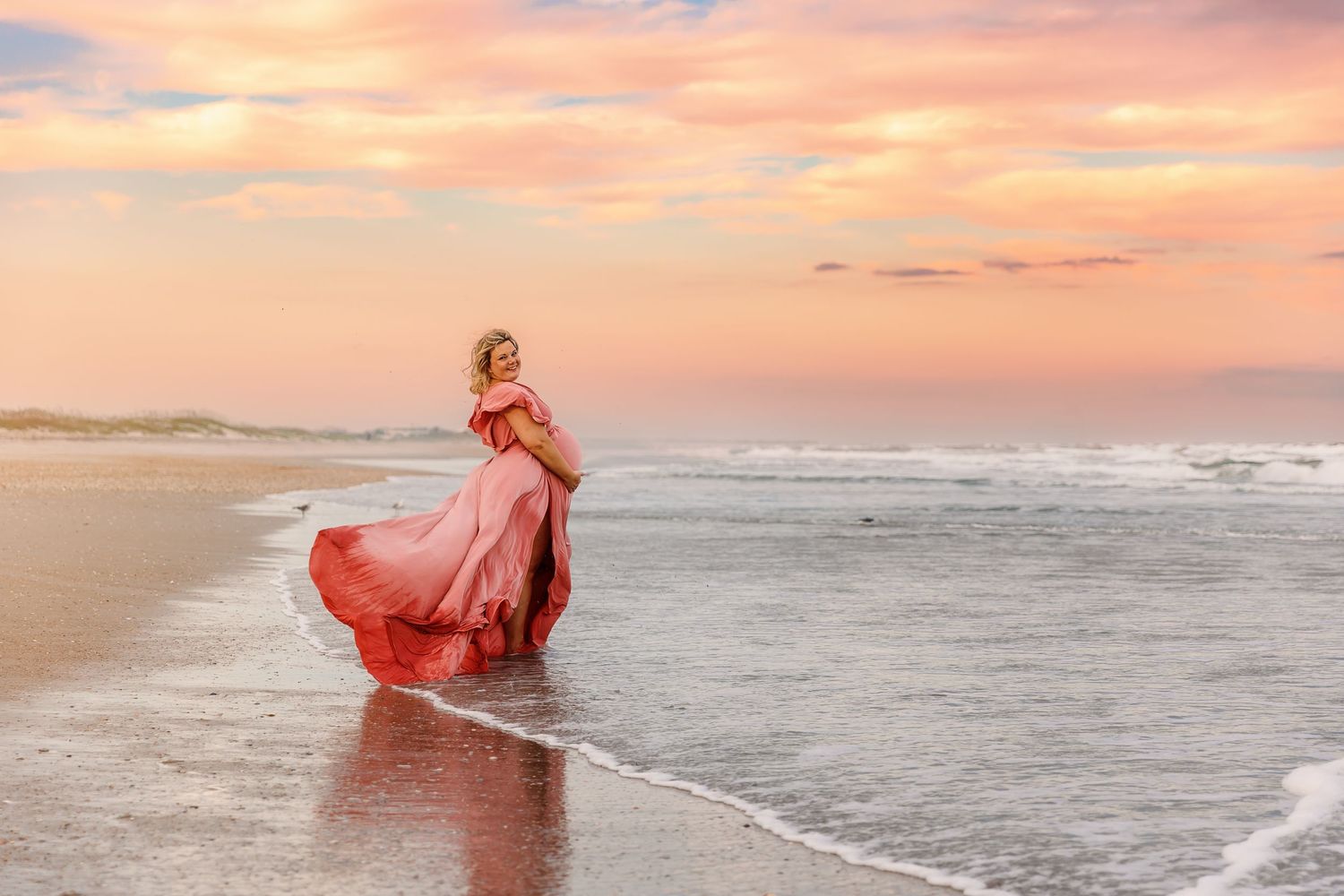 A coral dress at sunset on a beach with waves rolling on shore. Maternity session at Wrightsville Beach captured by Samantha Ann Photography
