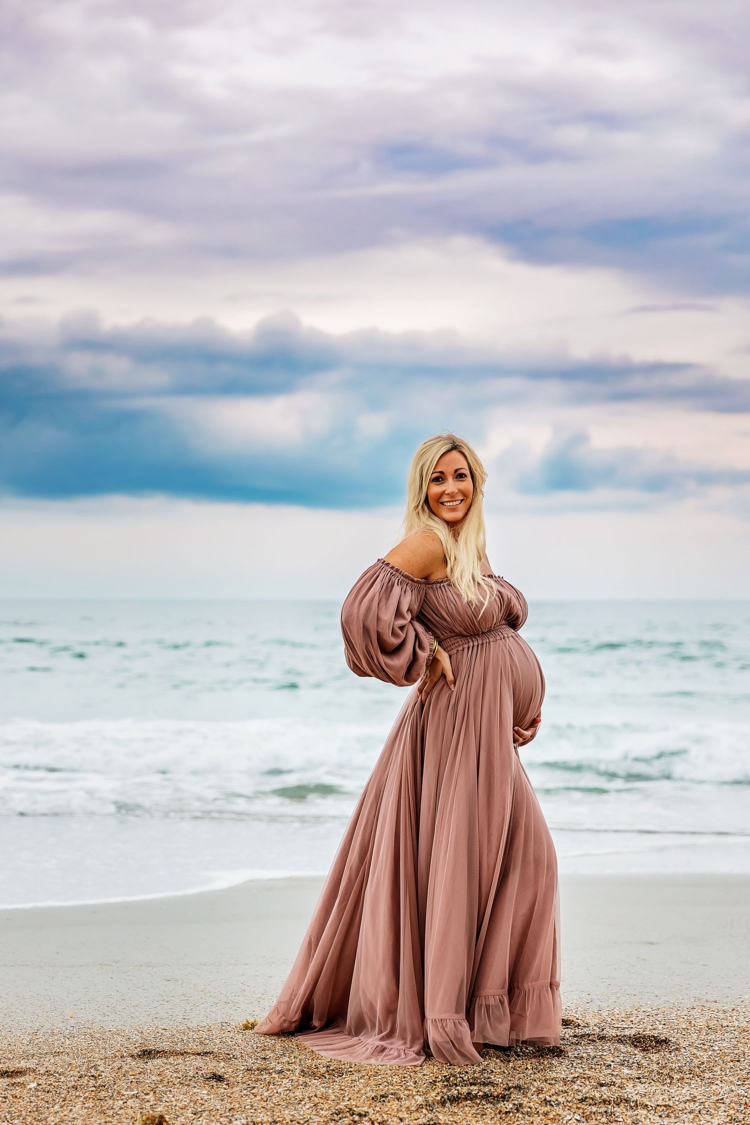 A mauve maternity gown on a beach with ocean waves. Maternity session at Wrightsville Beach captured by Samantha Ann Photography