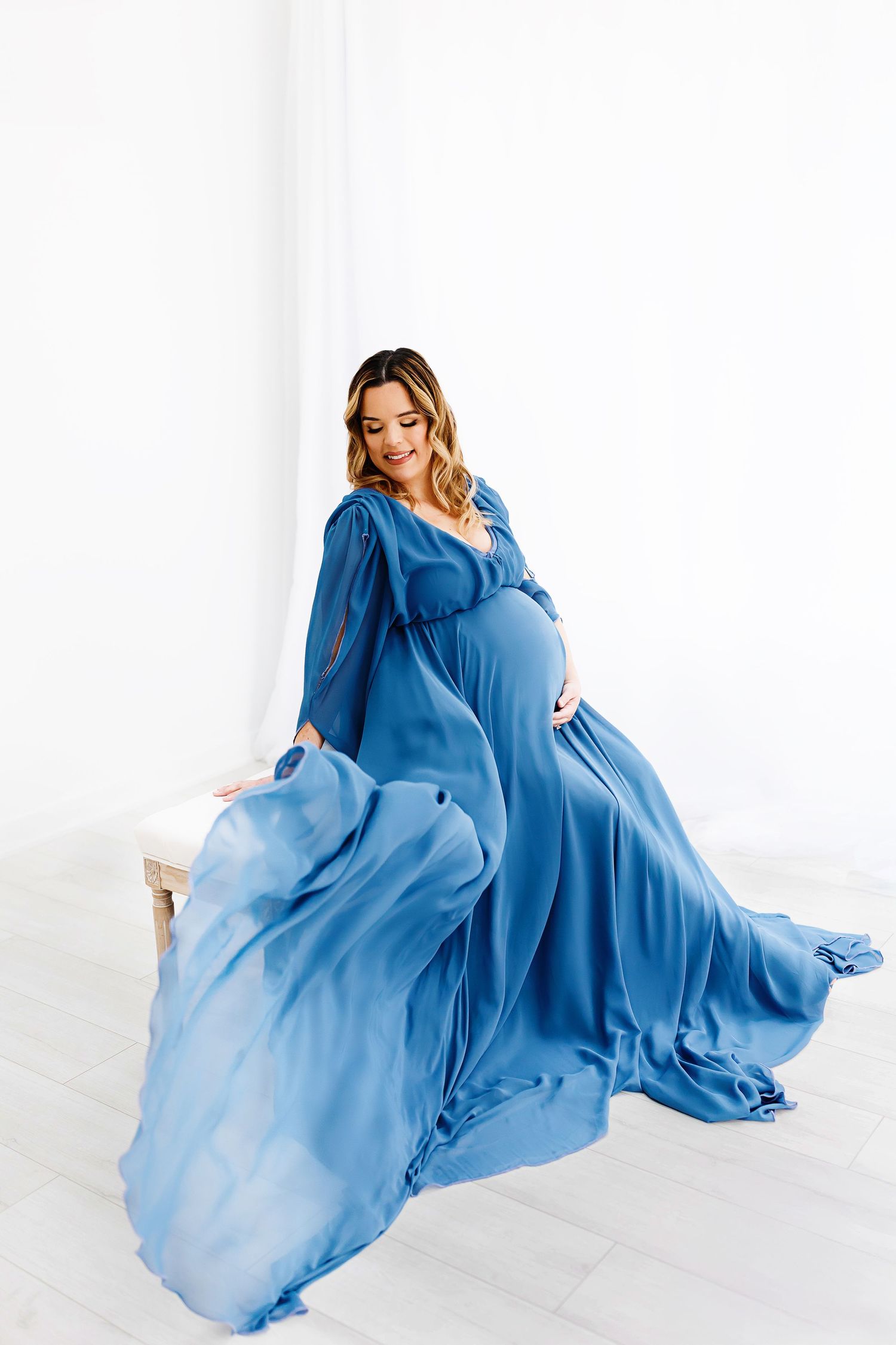 A blue maternity dress falling gracefully in a maternity session in the all-white natural light studio, captured by Samantha Ann Photography