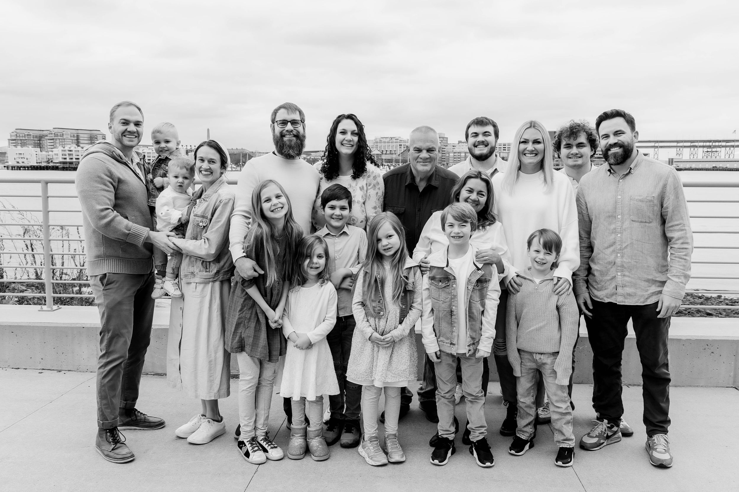 Black and white portrait of extended family gathering on coastal boardwalk.