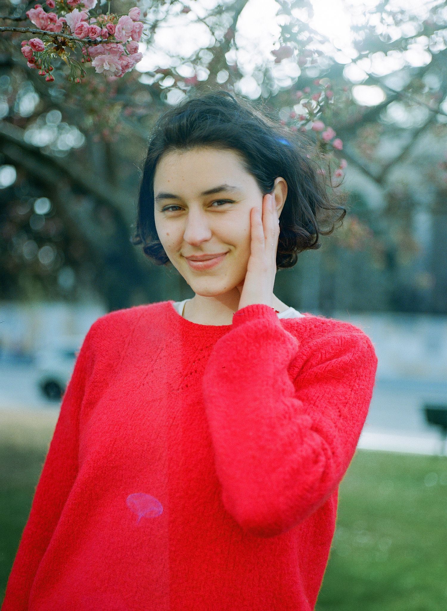 Person in bright red sweater poses outdoors with cherry blossoms in background.