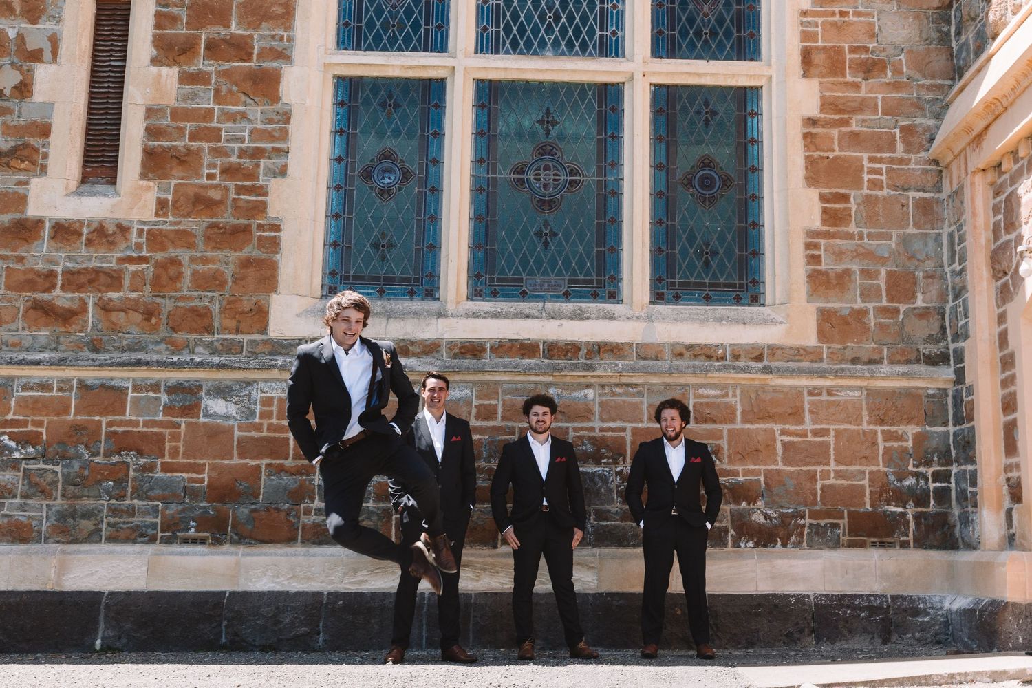 Four people stand outside a historic brick church building with leaded glass windows.