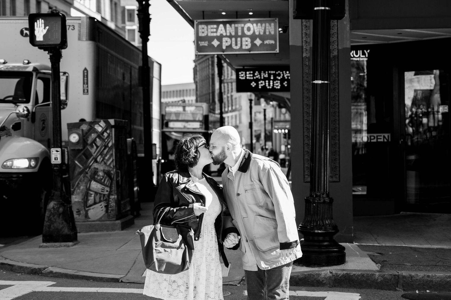 A black and white photo of a couple near a pub sign in an urban setting.