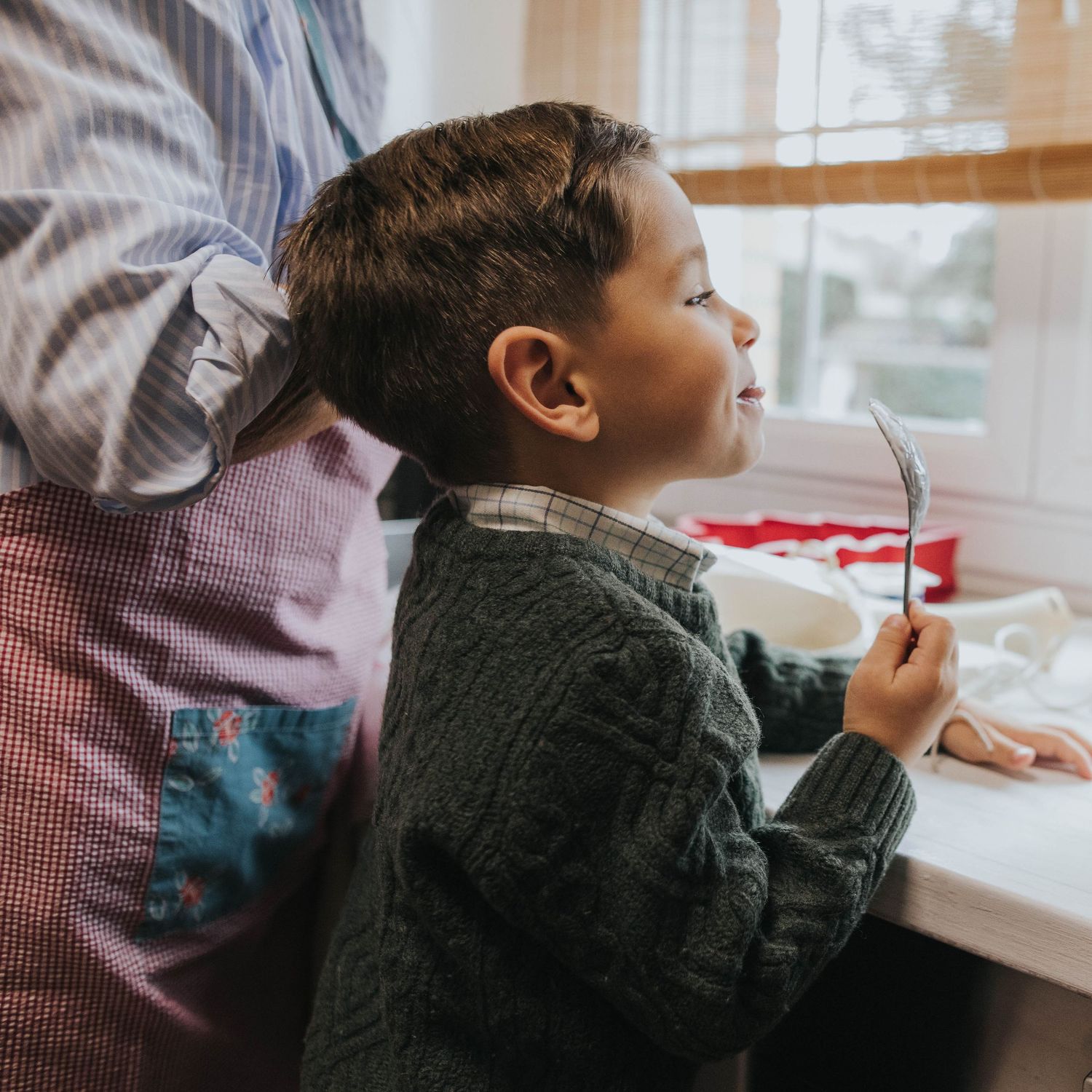 fotografia documental de navidad. nino chupando la cuchara mientras prepara bizcocho con sua abuela.