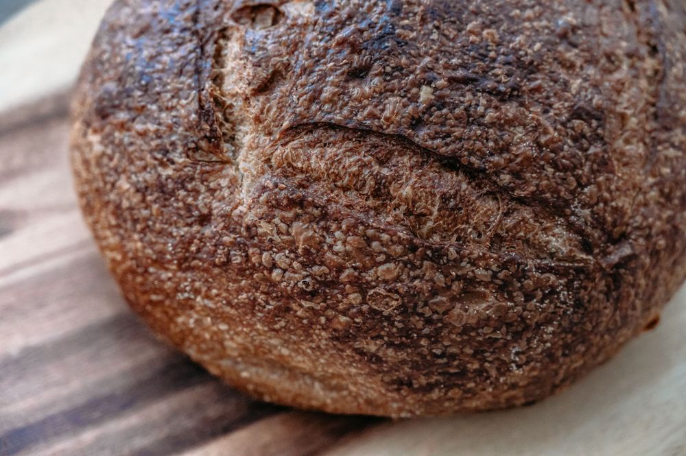 Artisanal dark sourdough bread with rustic crust on wooden surface by Sonoma. SIX84 Photography, Event Photography, Sydney