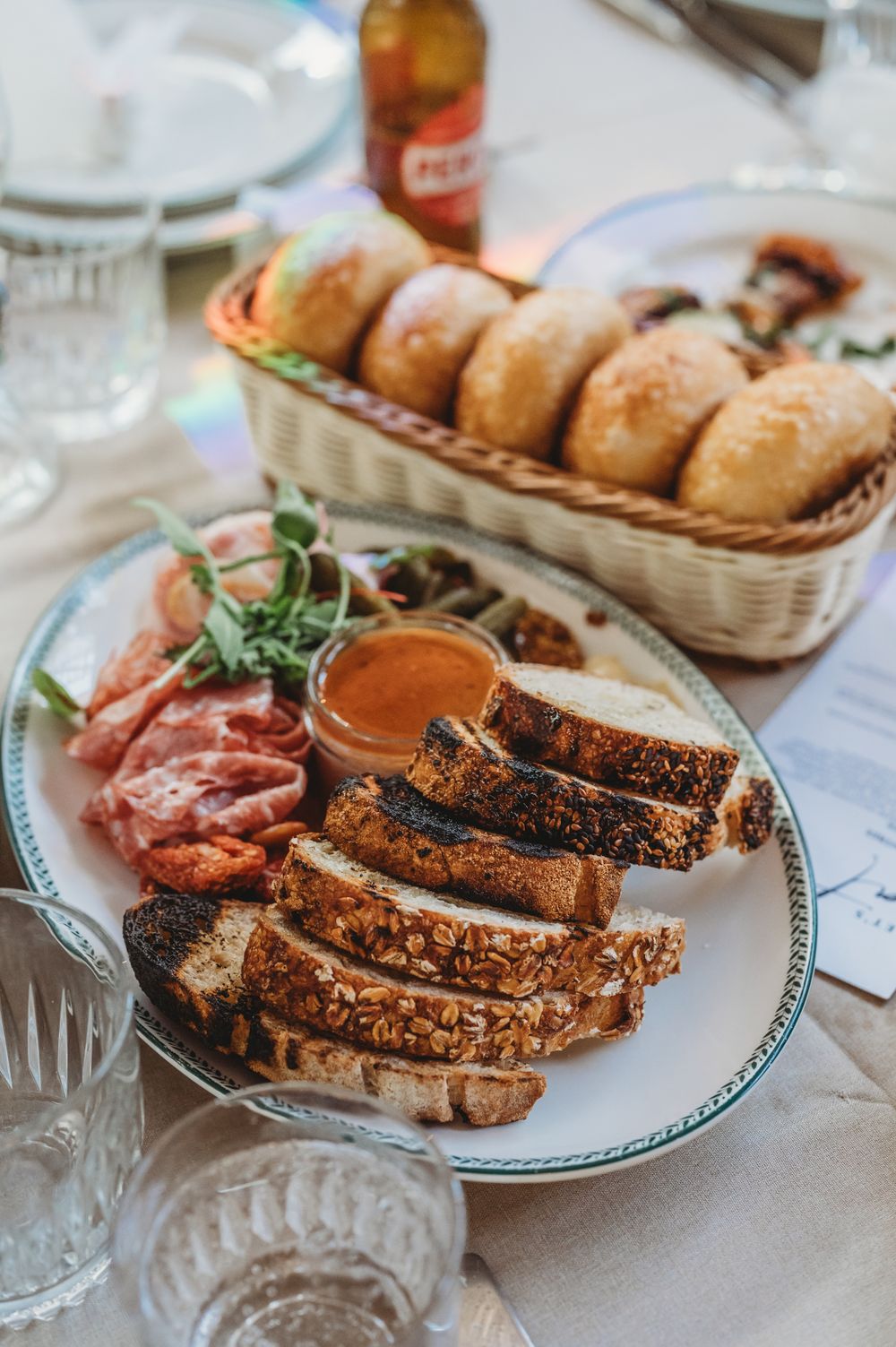 Sliced grilled meat on a decorative plate with sauce and fresh bread rolls in a woven basket. SIX84 Photography, Event Photography, Sydney