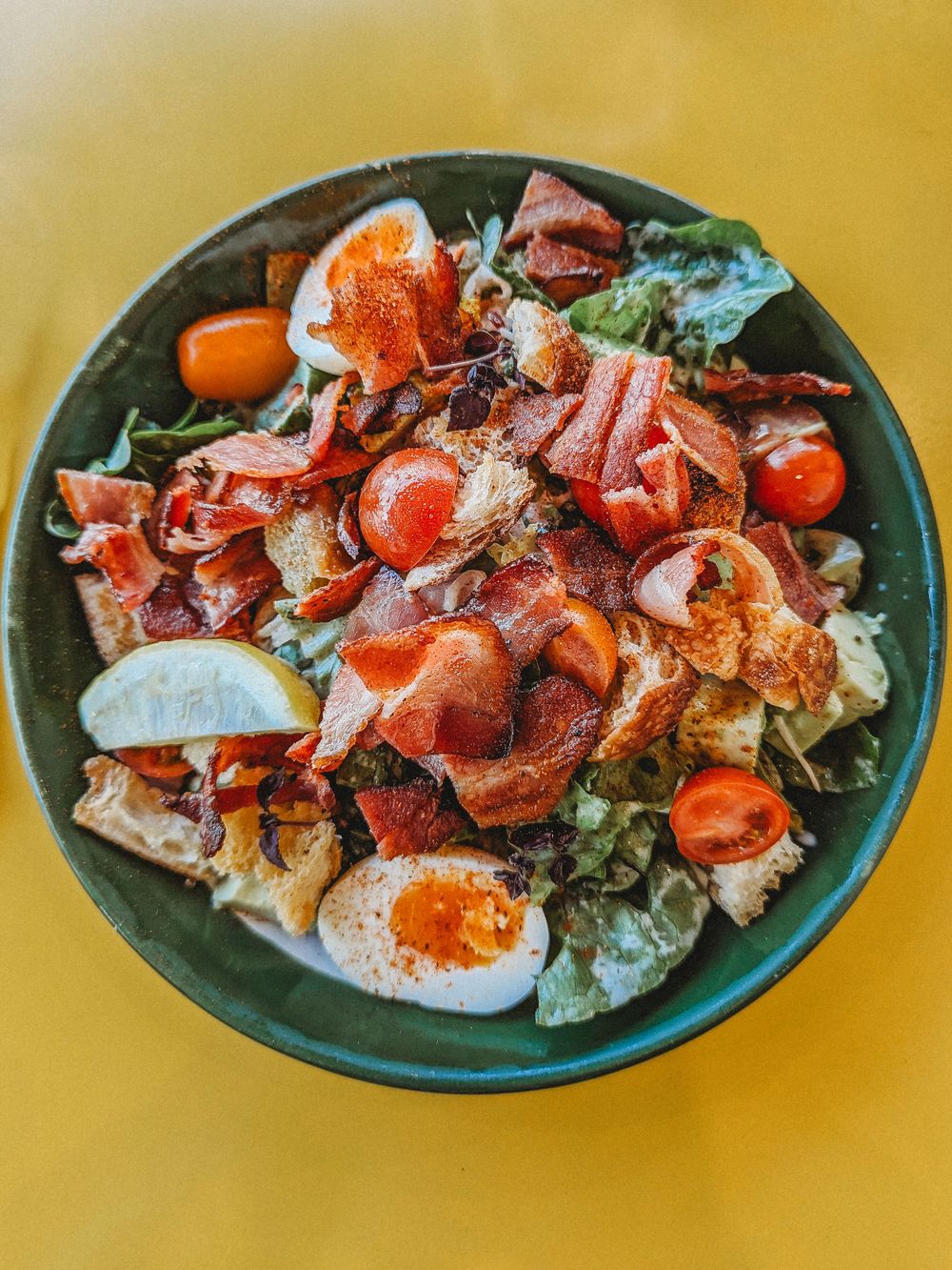 Colorful salad bowl with eggs, tomatoes, and bacon on yellow background at Happyfield. SIX84 Photography, Event Photography, Sydney