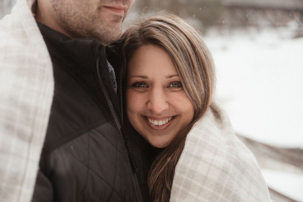 A cozy winter engagement photo of a couple sharing a warm embrace outdoors.
