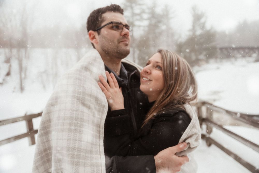 A joyful couple wrapped in a blanket share an intimate moment during their winter photoshoot.