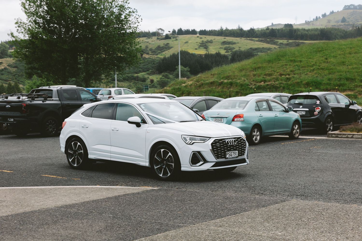 White Audi Q3 Sportback parked in a parking lot with hills in the background.