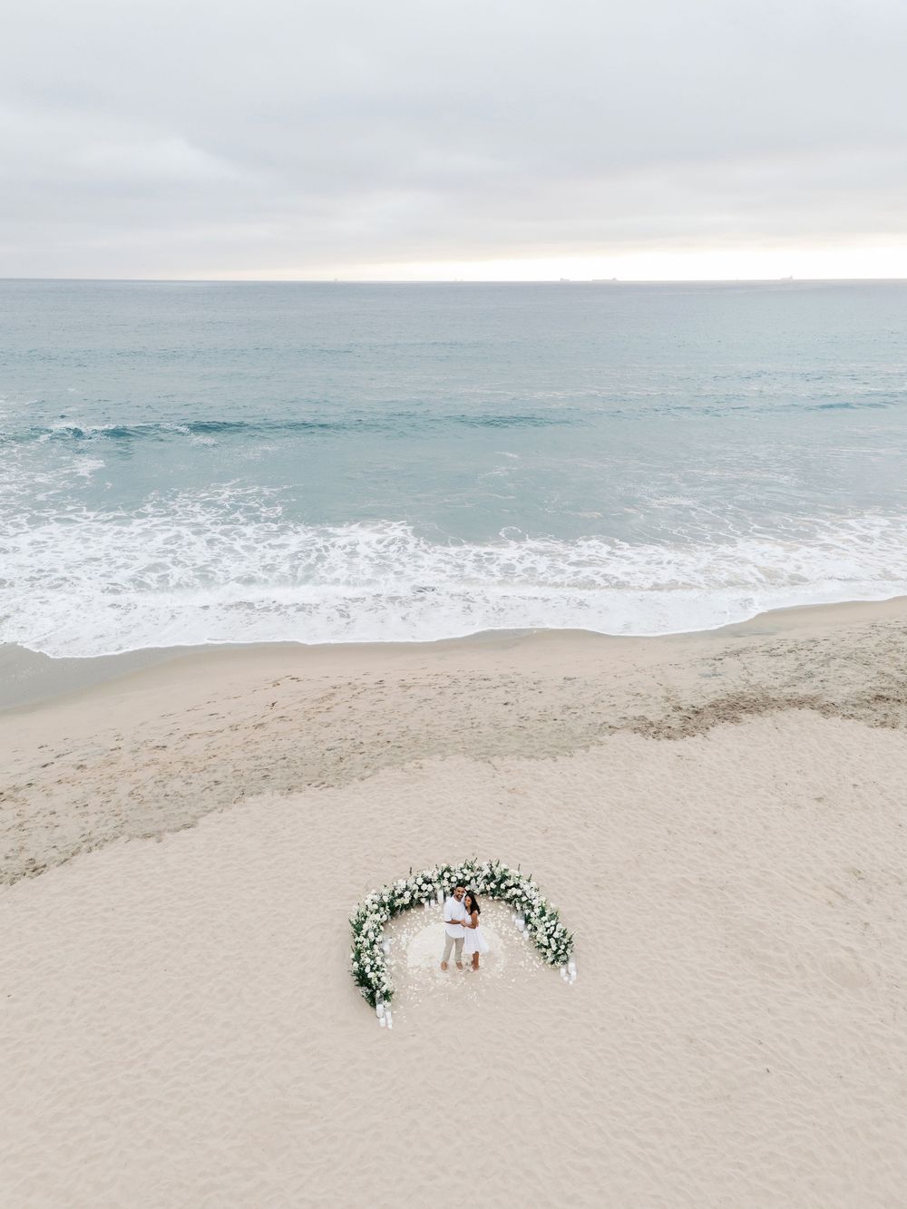 Floral arch installation on a serene beach with multiple arrangement setups along the sandy shoreline.