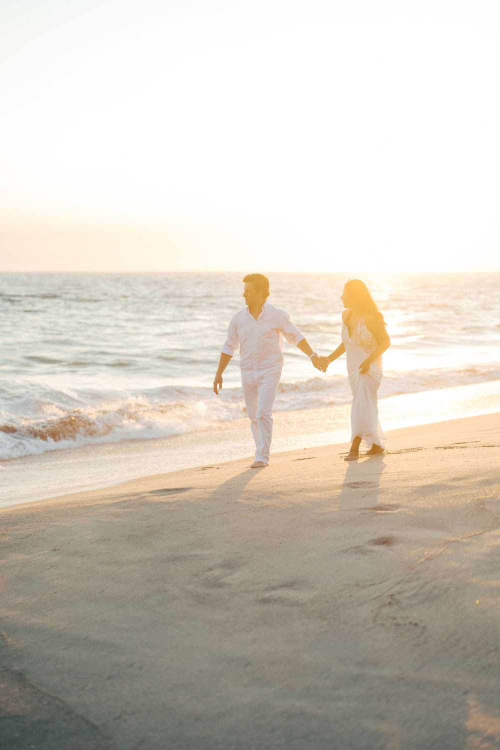 Silhouettes of a couple walking along a sandy beach during golden hour.