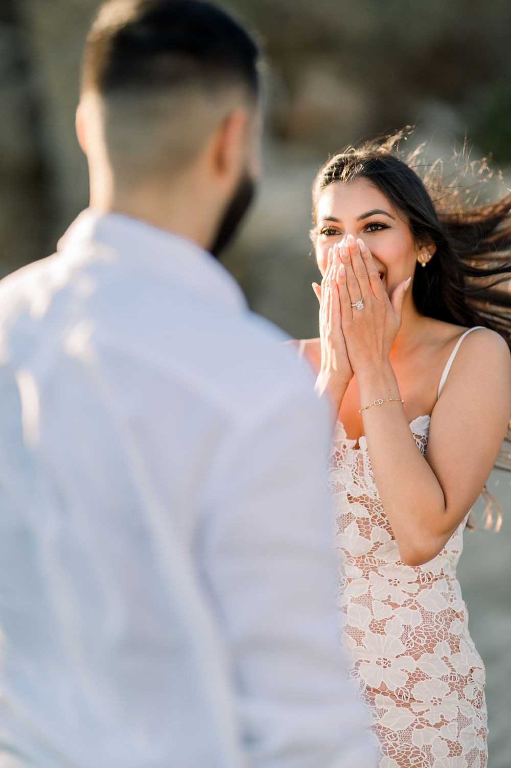 A surprised reaction captured during a romantic beach proposal with sunlit backlighting.