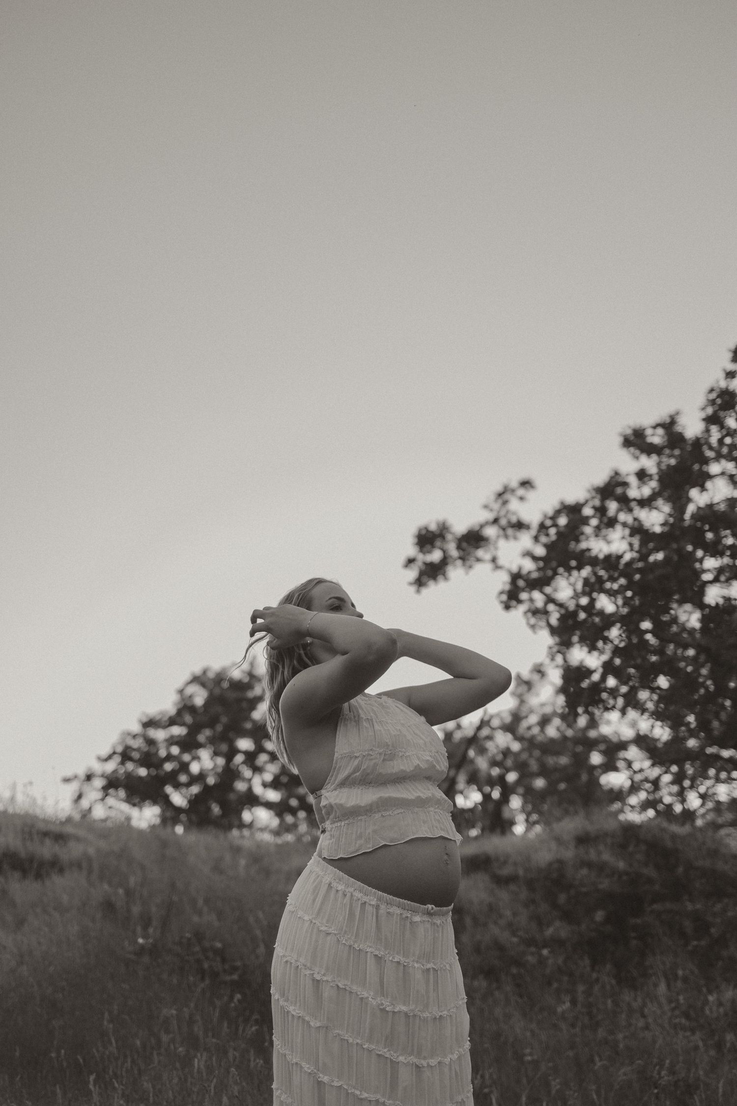 Four sequential black and white photos showing a person in a dress stretching and bending their upper body outdoors.