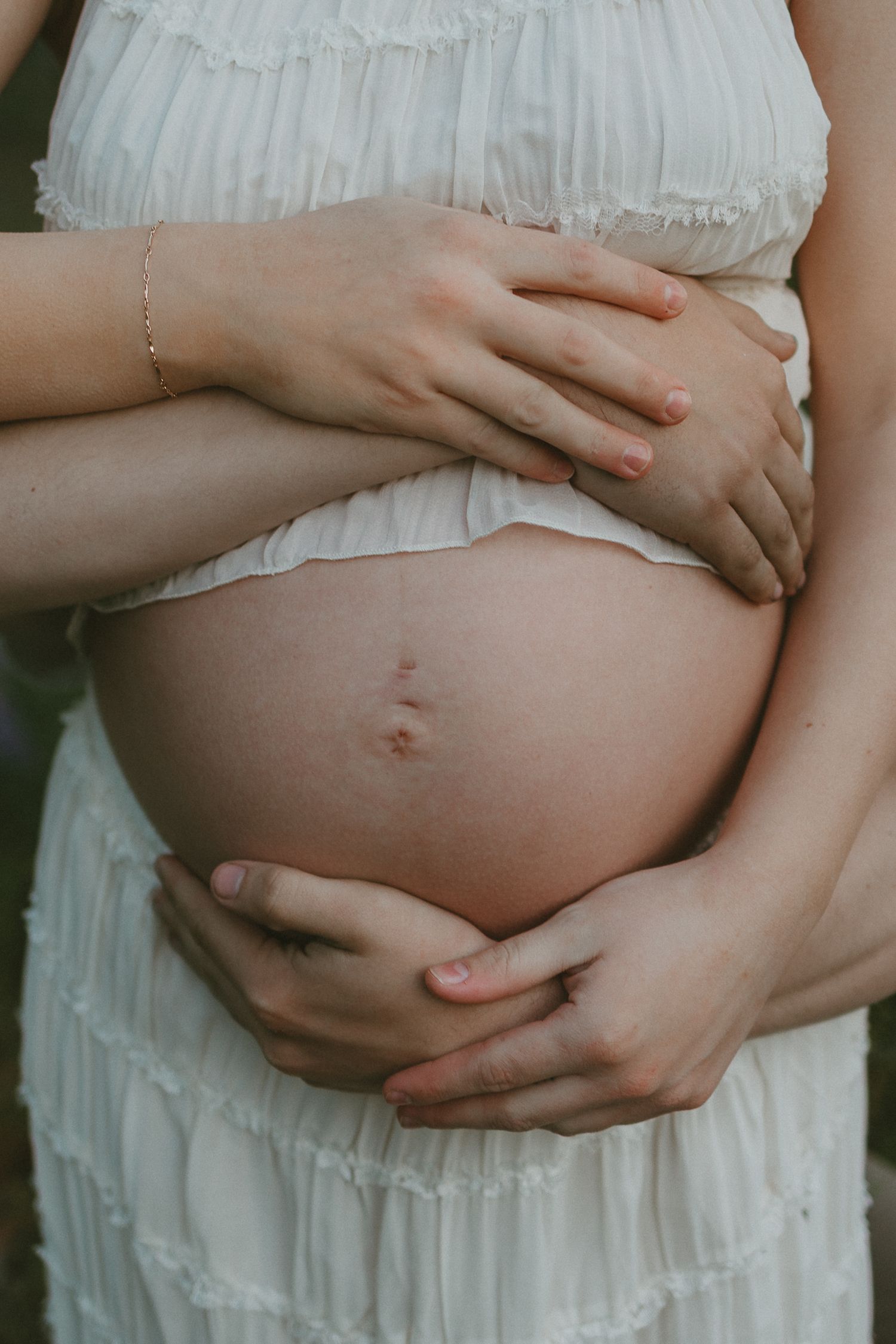 A sequence of pregnancy belly progression photos showing hands cradling a growing baby bump in a white dress.