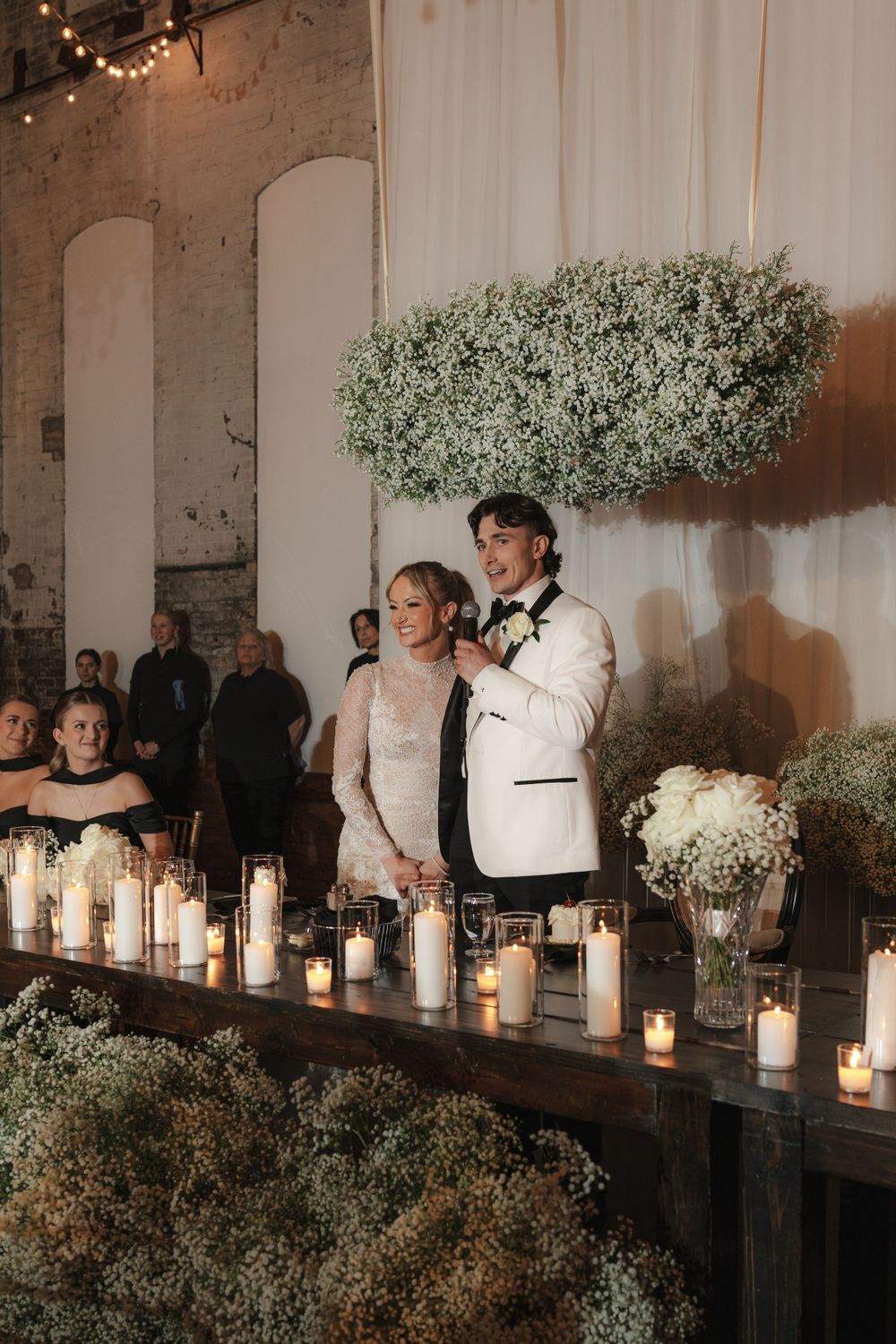 Wedding reception decor with baby's breath arrangements and glowing candles against industrial backdrop.