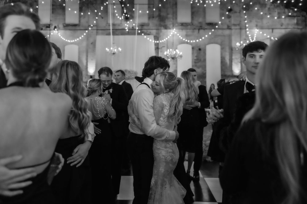 Black and white photo of couples dancing at an elegant reception with string lights overhead.