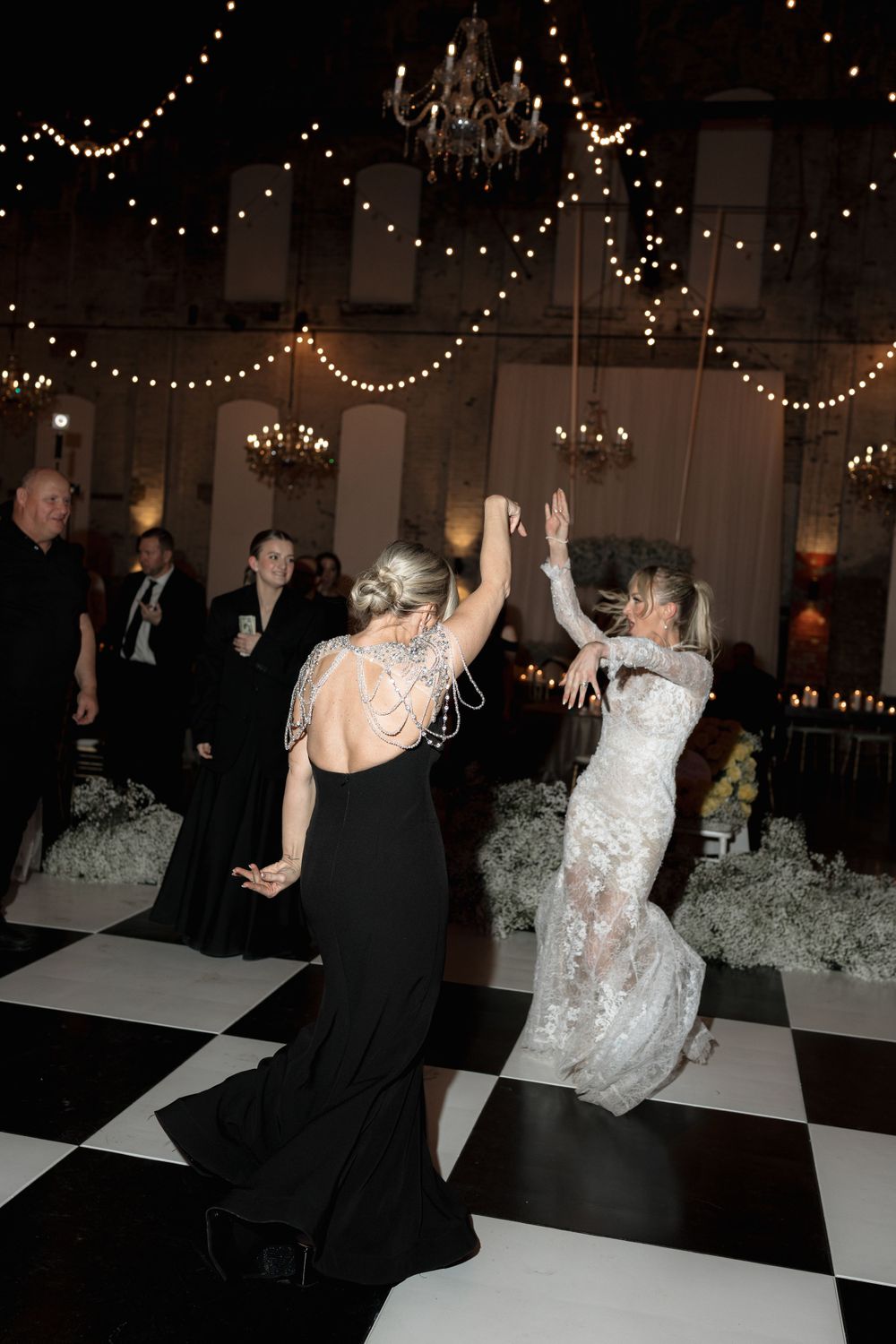 Wedding guests dancing enthusiastically on a checkered dance floor under twinkling reception lights.