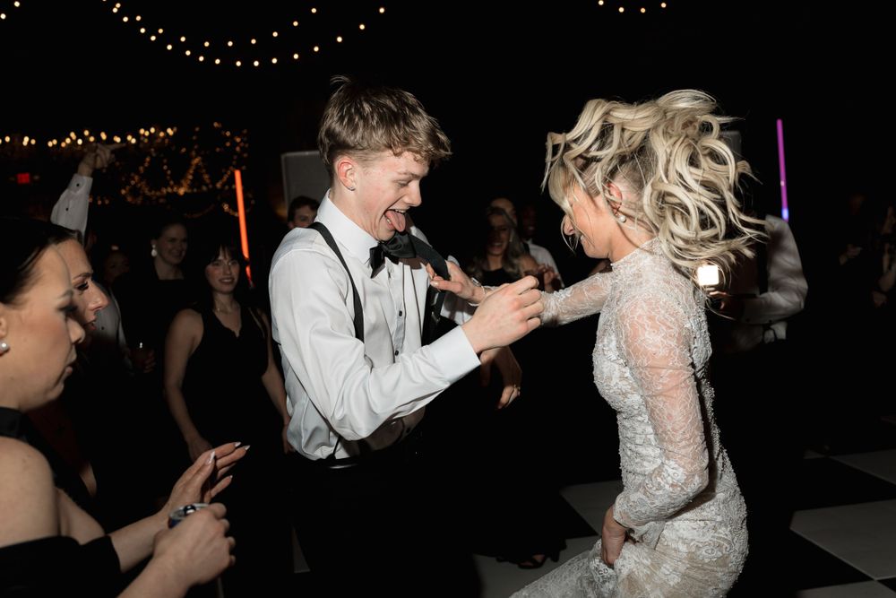 Wedding guests dancing energetically on the reception dance floor under atmospheric lighting.