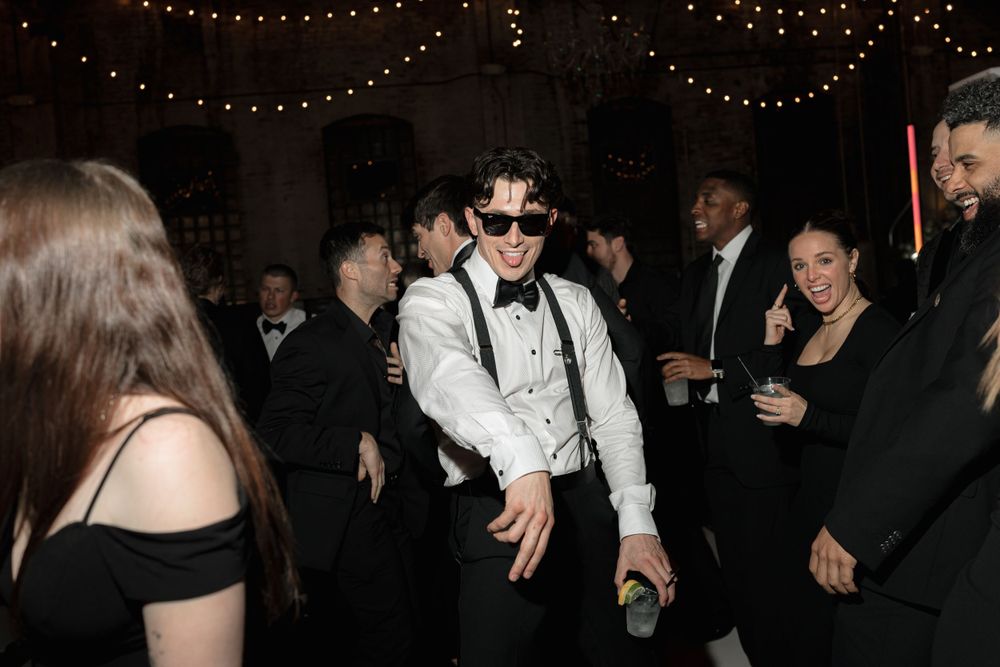 Party guests dancing at a wedding reception with string lights overhead and a festive atmosphere.
