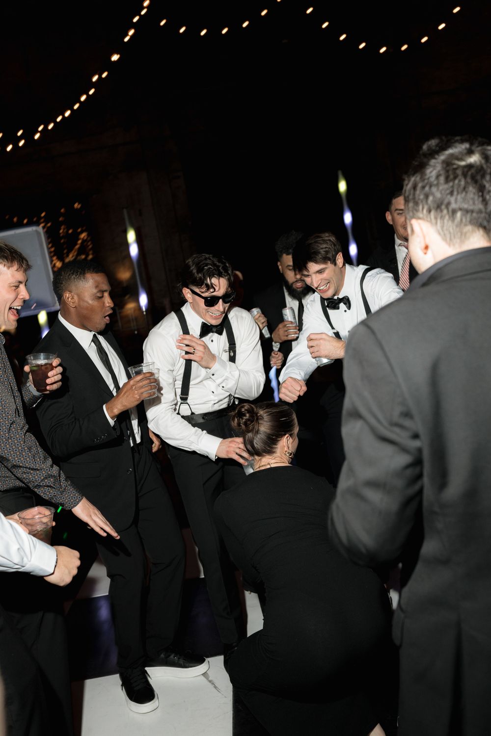 Formal party guests gathered in a circle during an evening celebration under string lights.