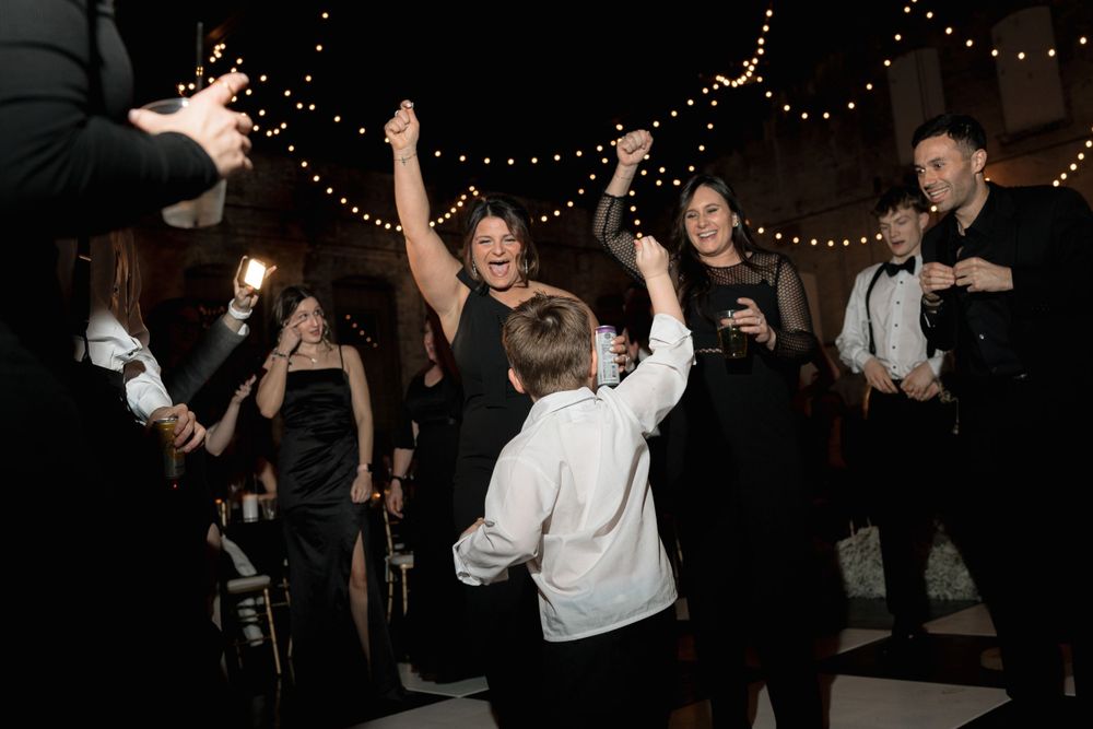 Lively dancing and celebration at a formal event with string lights overhead.