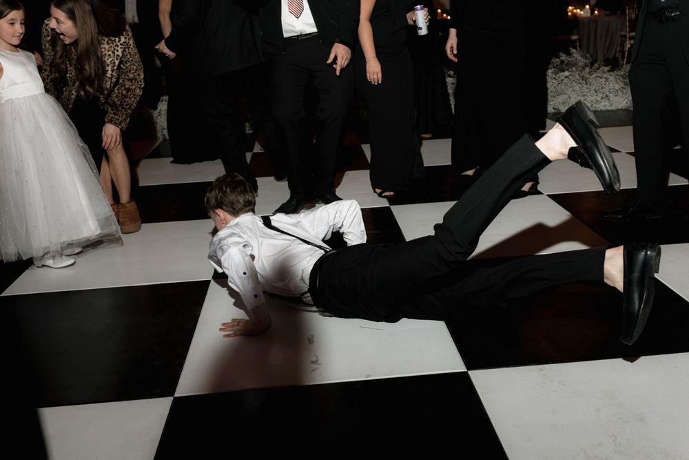 Someone lying on a black and white checkered dance floor during a formal celebration.