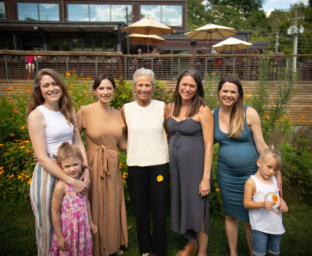 A group poses together for a portrait in a garden with patio umbrellas visible behind them.