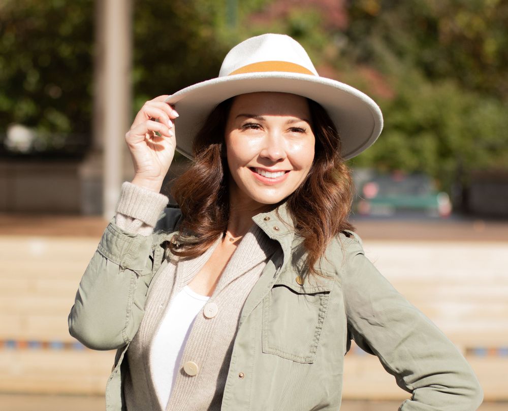 Natural lifestyle portrait in sage jacket and cream fedora hat outdoors.