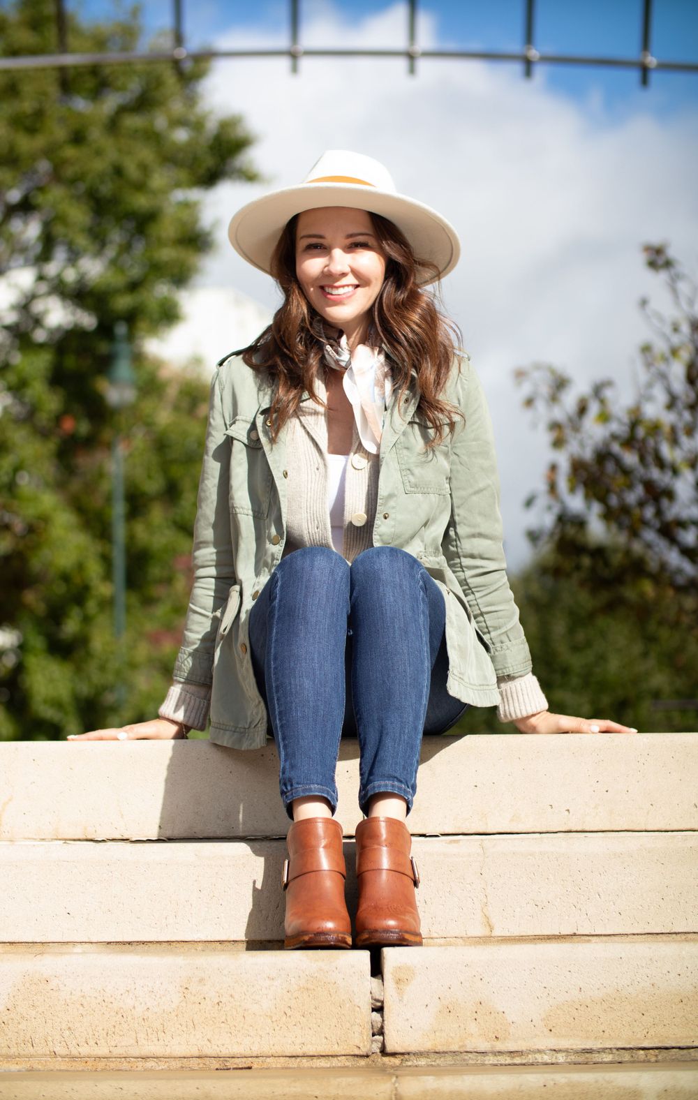 Relaxed outdoor portrait on concrete steps wearing utility jacket and brown ankle boots.
