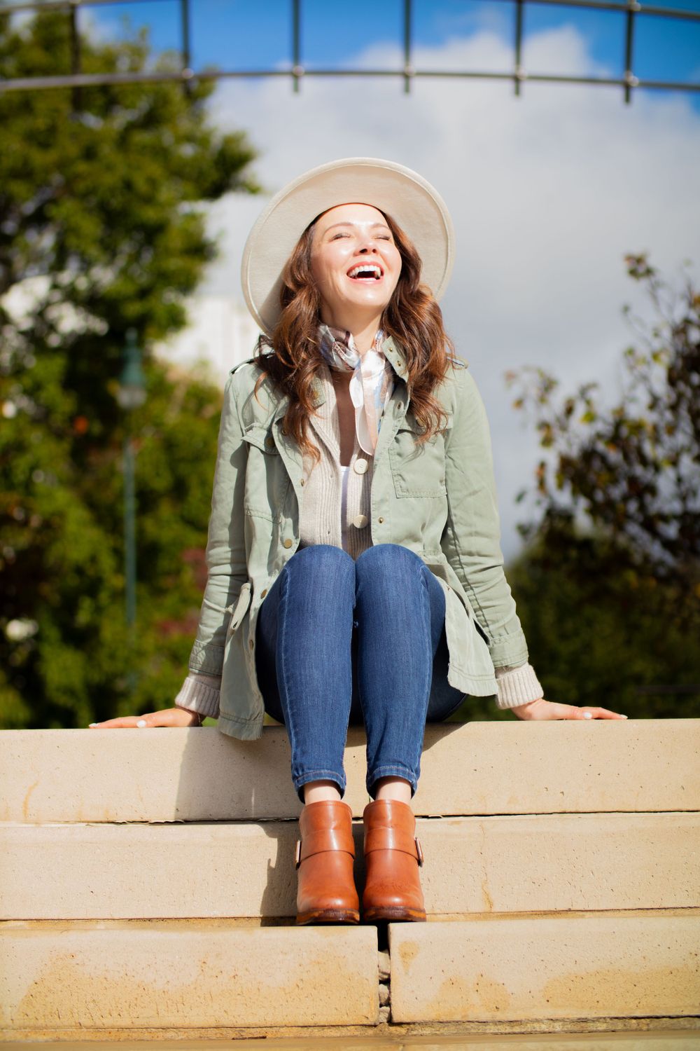 Joyful autumn fashion portrait on concrete steps with fedora hat and olive jacket.