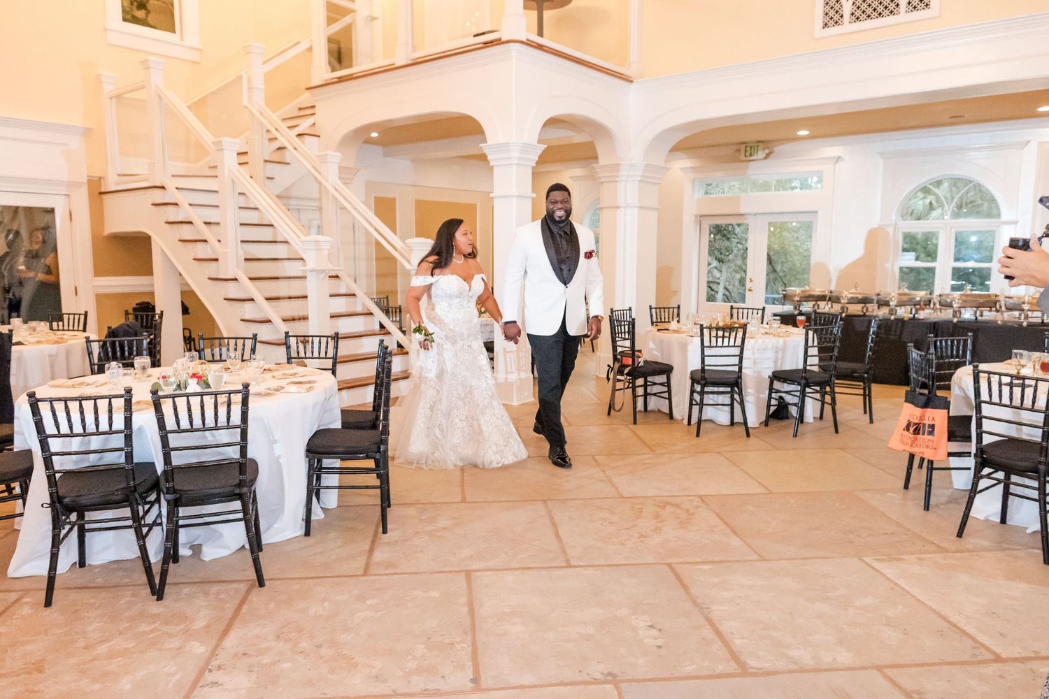 A couple shares an intimate moment in an elegant reception venue with white arches and Chiavari chairs.