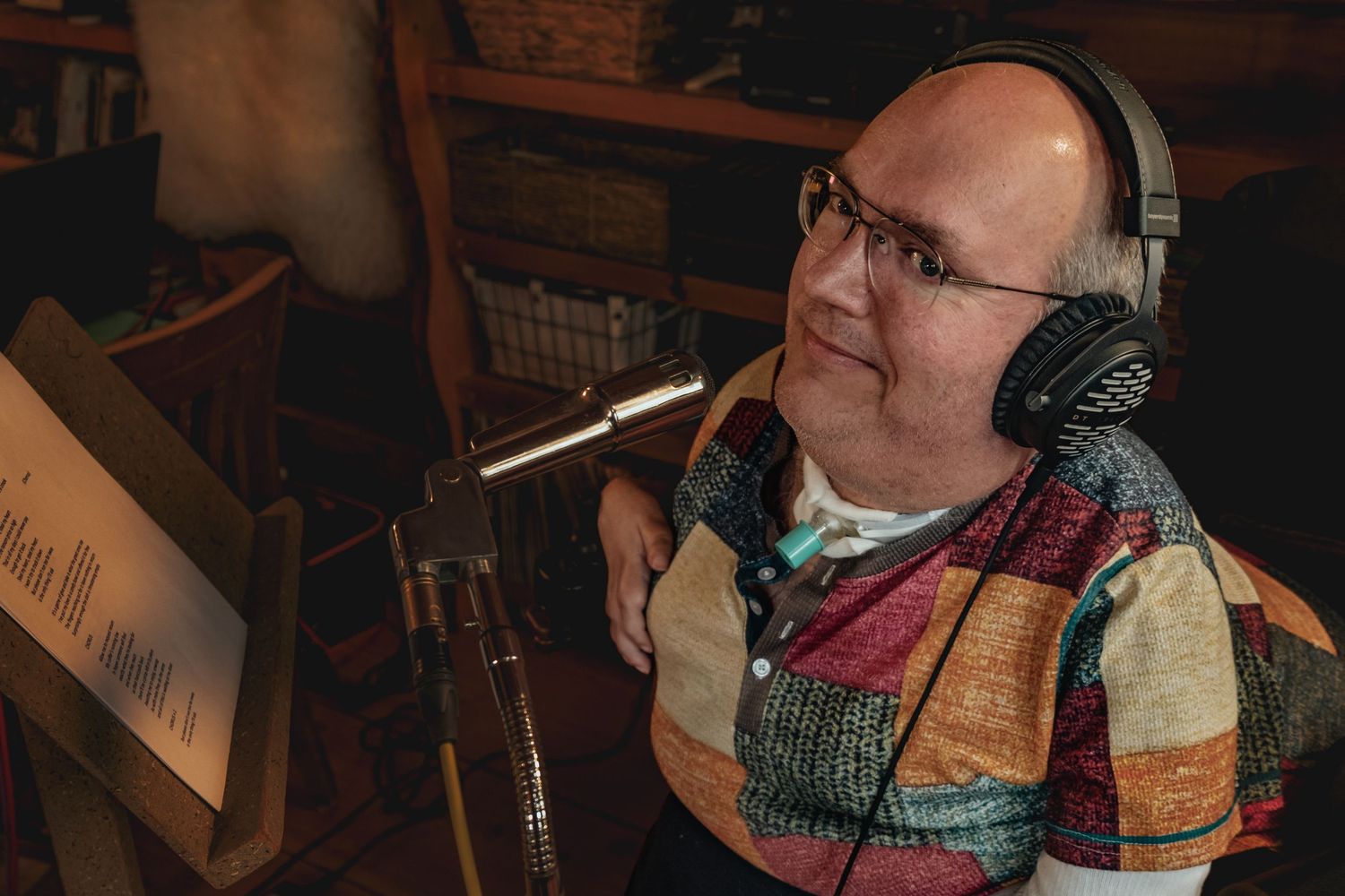 Person wearing a colorful sweater and headphones works at what appears to be a recording or production station.
