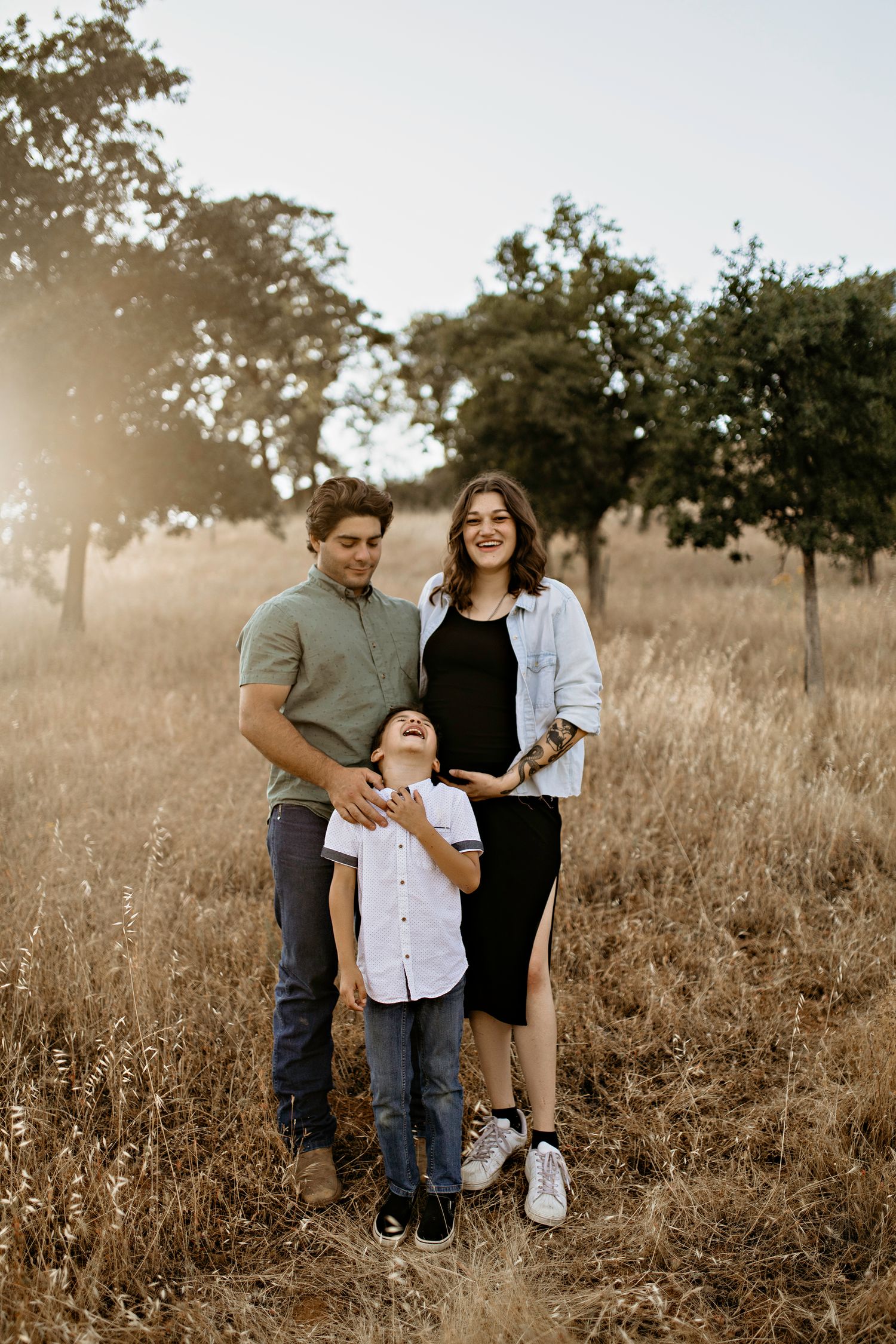 A family poses together in a golden field at sunset with trees in the background for family portraits in El Dorado Hills