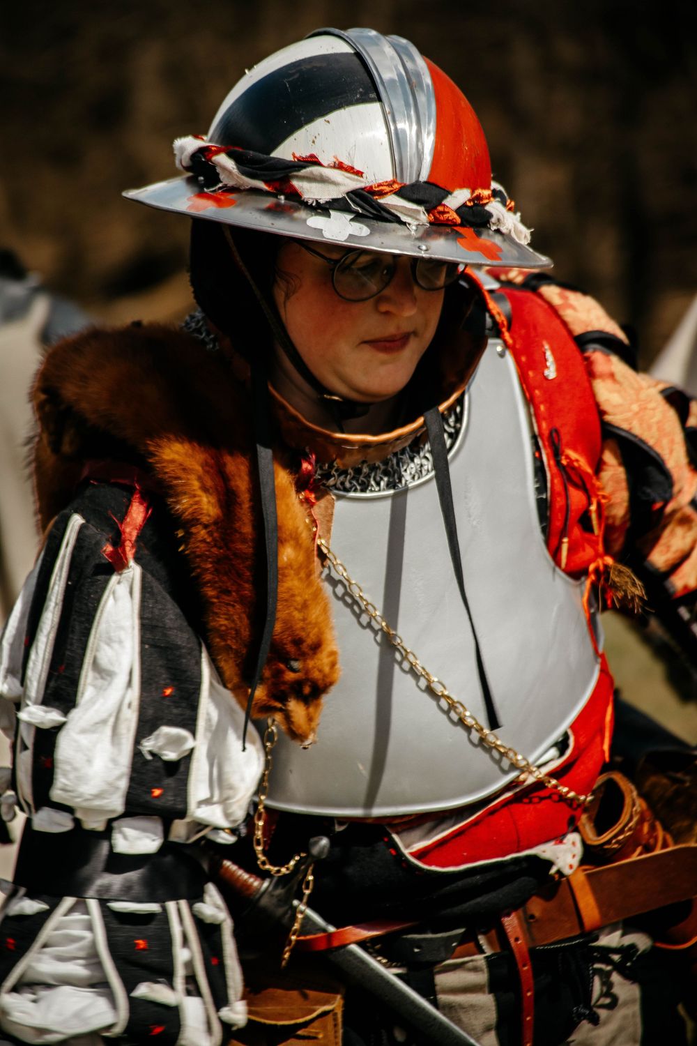 Medieval reenactor wearing ornate armor, feathered helmet and fur trim at a historical costume event.