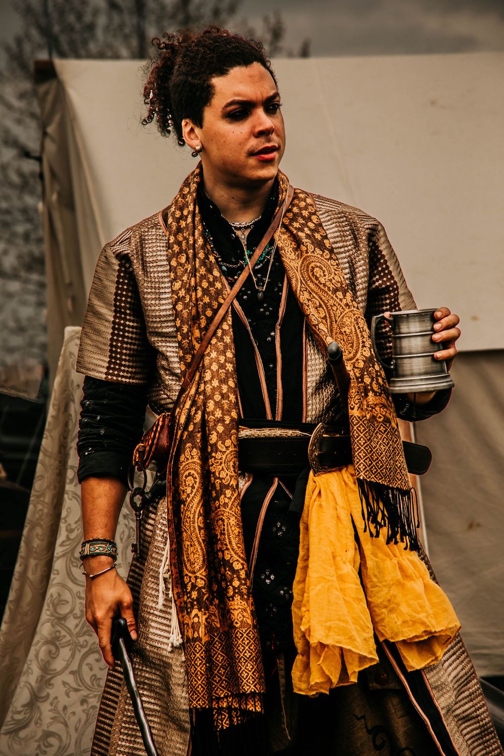 A portrait of someone at a renaissance fair wearing layered medieval-style clothing with a patterned scarf and knit coat.