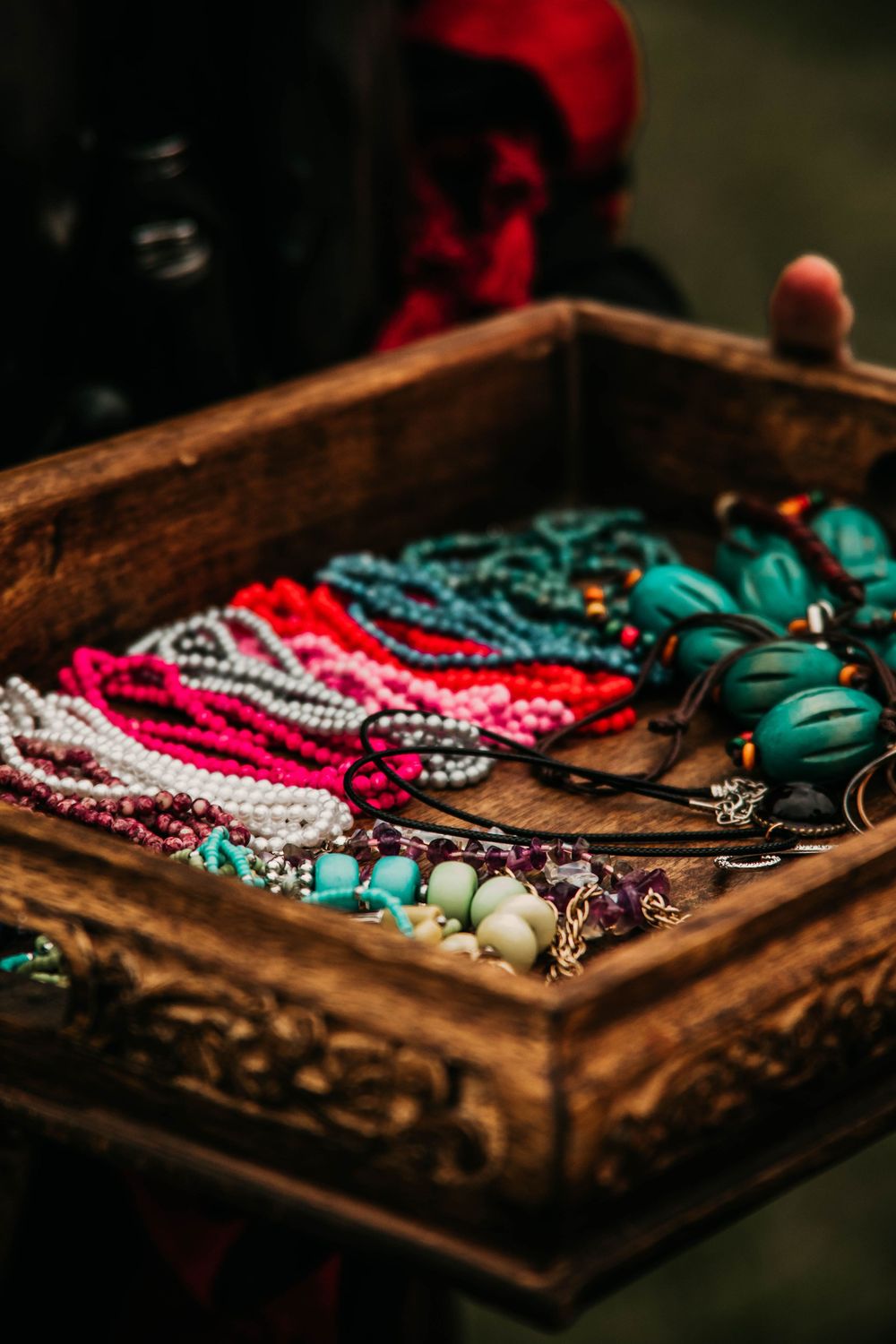 Colorful beaded necklaces and turquoise jewelry displayed in rustic wooden box at vintage market.