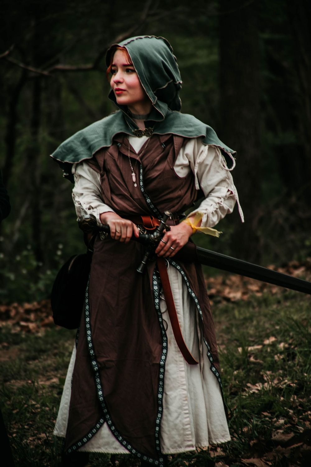 Medieval-inspired costume with brown tunic, white dress and green hood in a forest setting.