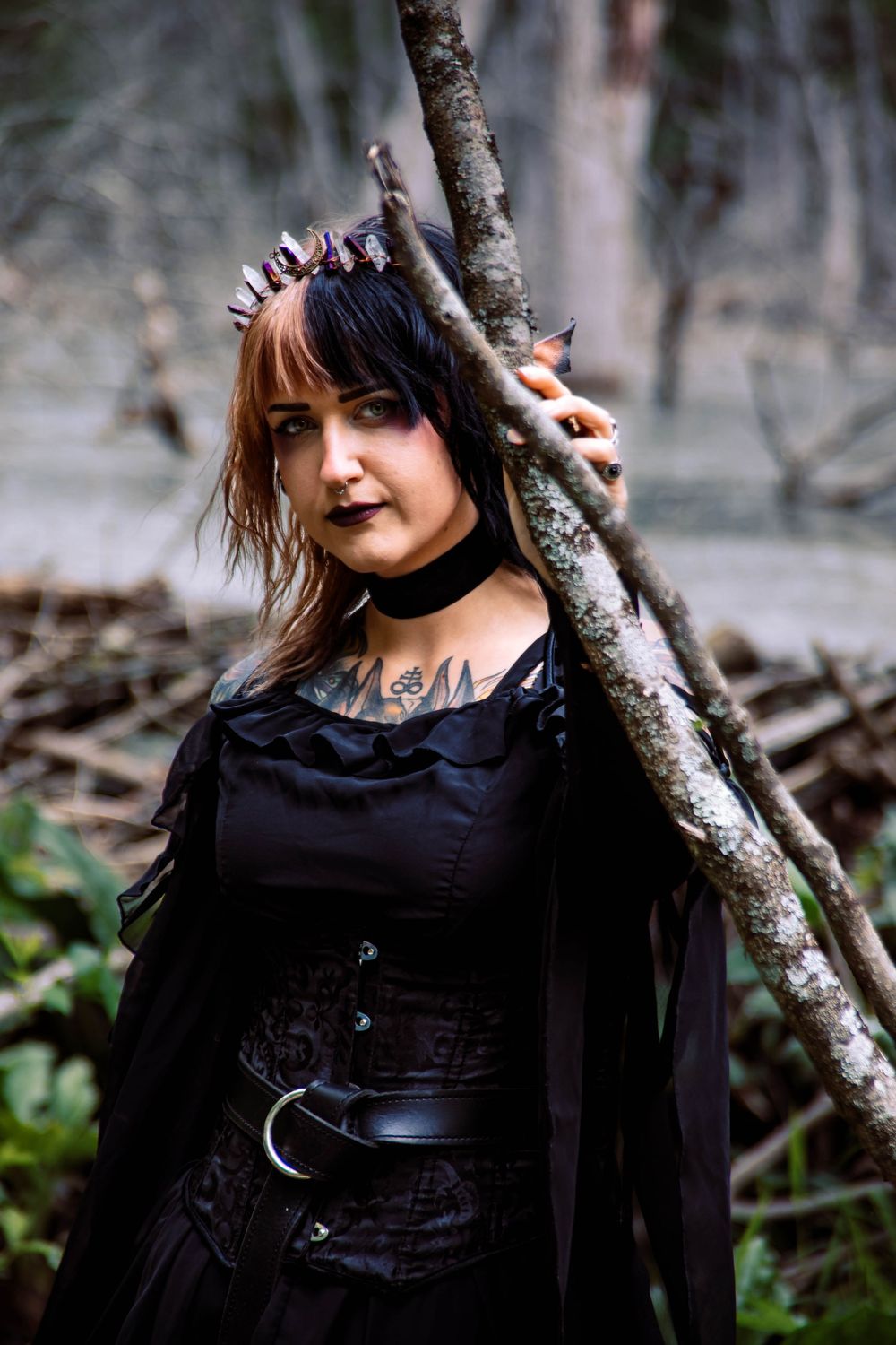 Gothic style in a forest setting with dark clothing, spike crown, choker and corset in a moody atmosphere.