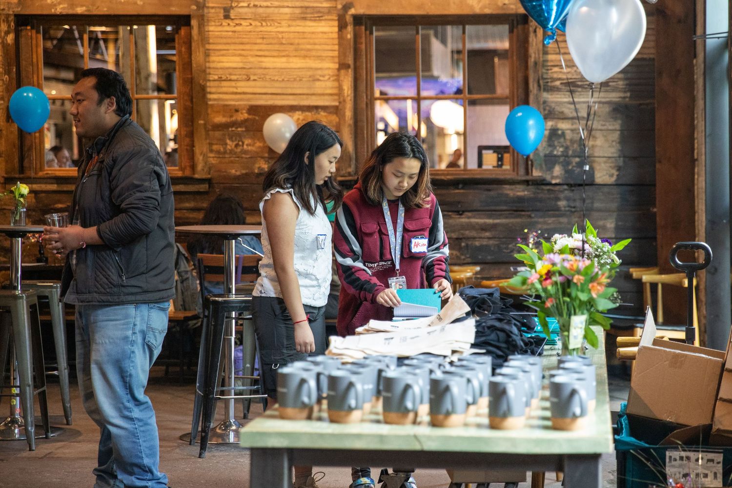 People gather around a table with a birthday cake and decorations in a rustic wood-paneled restaurant setting.