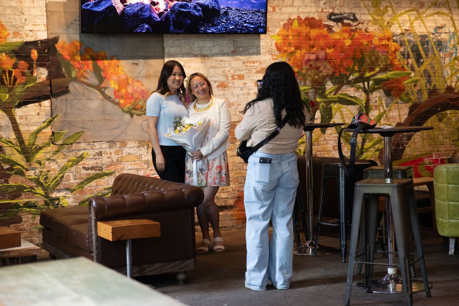 Three people standing in a casual restaurant setting with exposed brick walls and autumn decor.