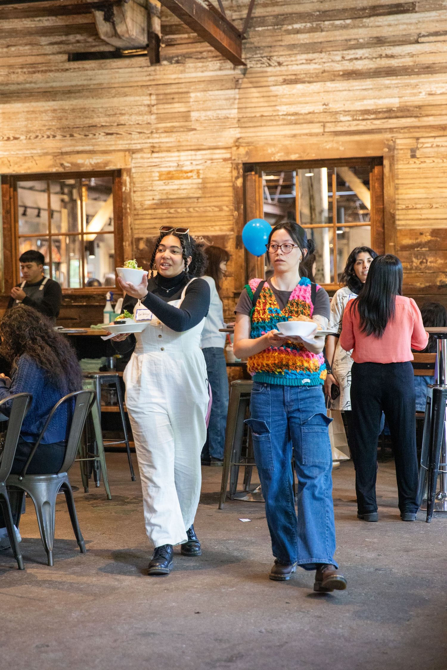Casual diners enjoy a rustic restaurant interior with wooden walls and metal chairs in an industrial-style space.