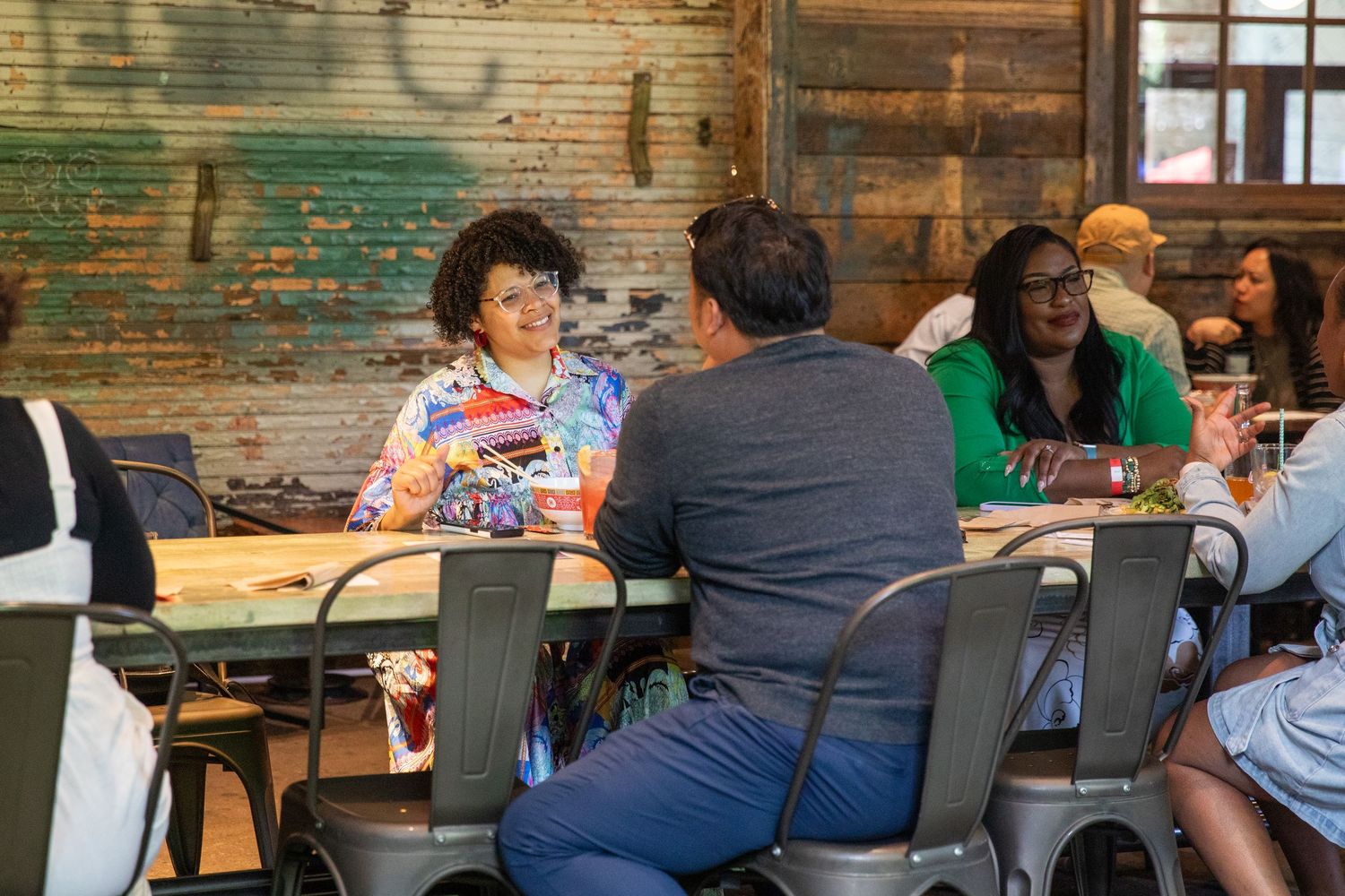People seated at tables having conversations in a rustic restaurant with wooden walls and industrial decor.