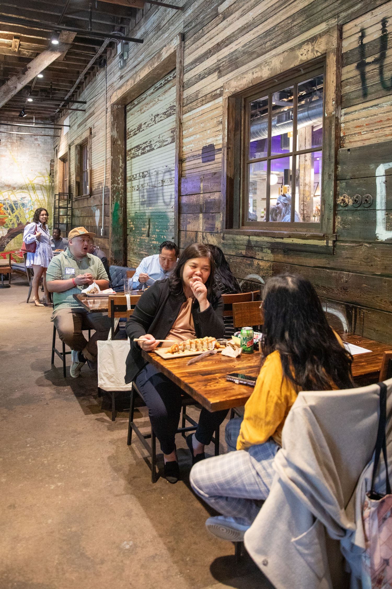 Diners enjoy a casual meal at rustic restaurant with weathered wood walls and industrial urban atmosphere.